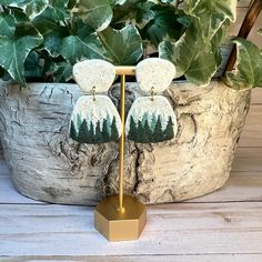 a pair of earrings sitting on top of a wooden stand next to a potted plant