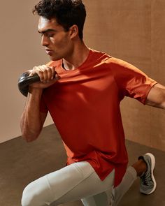 a man in an orange shirt and white pants is holding a black object with one hand