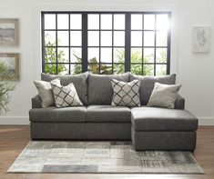 a living room with a large gray couch and pillows on the floor next to a window