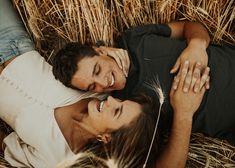 a man and woman laying on the ground next to some hay with dandelions