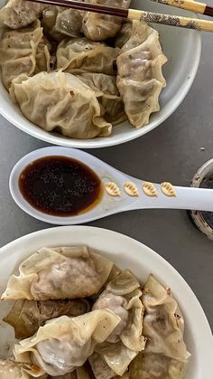 two white bowls filled with dumplings and sauce next to chopsticks on a table