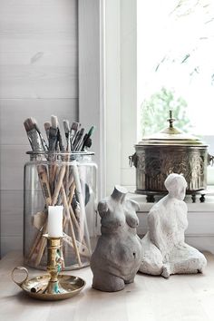 two statues sitting on top of a wooden table next to a jar filled with brushes