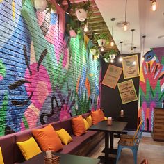 a colorful mural on the wall of a restaurant with wooden tables and chairs in front of it