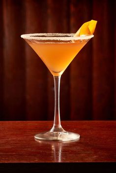 an orange cocktail in a martini glass with a lemon wedge garnish on the rim