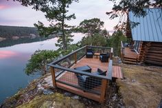 a wooden deck with chairs on it next to a body of water and trees in the background