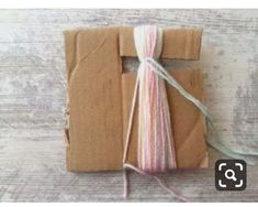 a piece of brown paper with pink, white and blue yarn on top of it