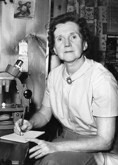 a woman sitting at a desk writing on a piece of paper in front of a microscope