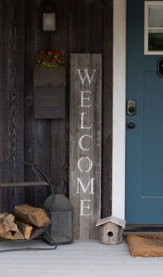 a welcome sign sitting on the front porch next to a pile of firewood and a birdhouse