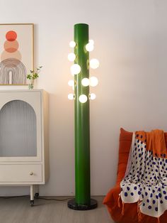 a green lamp sitting next to a white cabinet in a room with orange and blue pillows