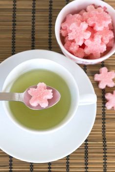 a cup of green tea with pink sugar cubes in it and a spoon on the side