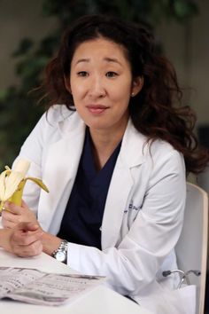 a woman sitting at a table with a banana in her hand and papers on the table next to her