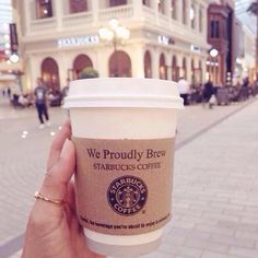 a person holding up a cup of coffee in front of a building on the street