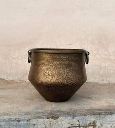 a large metal pot sitting on top of a cement slab next to a white wall