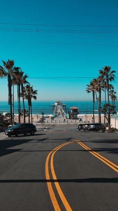 the road is lined with palm trees on both sides and an ocean in the background