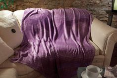 a couch covered in a purple blanket next to a cup and saucer on a table