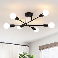 a black chandelier hanging from the ceiling in a room with white walls and curtains