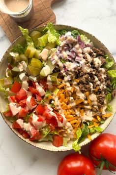 a salad with dressing in a bowl next to two tomatoes and a cup of coffee