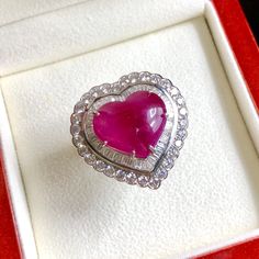 a pink heart shaped ring sitting in a red and white box on top of a table