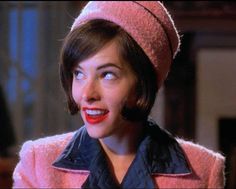 a woman with short hair wearing a pink coat and red lipstick in front of her face