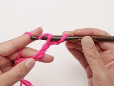 two hands crocheting the end of a piece of pink yarn