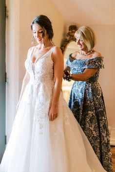 two women standing next to each other in front of a mirror wearing wedding gowns