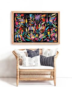 a painting hanging on the wall next to a wicker chair with pillows in front of it