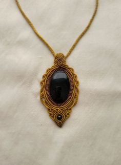 a gold necklace with a black stone in the center on a white cloth covered surface