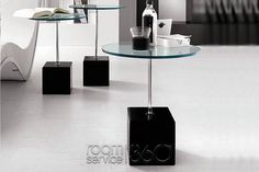 three glass tables with black bases on each side and one table that has a book in the middle