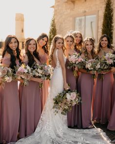 a group of women standing next to each other wearing dresses and holding bouquets in their hands