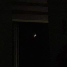 the moon is shining brightly in the dark night sky over a window with curtains on it