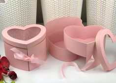 pink heart shaped boxes with ribbons and bows on white table cloth next to vases