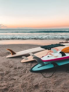 three surfboards are laying on the beach at sunset