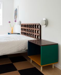 a white bed sitting next to a green and brown nightstand on top of a checkered floor