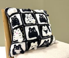 a black and white crocheted pillow with cats on it sitting on a chair