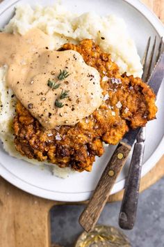 a white plate topped with mashed potatoes covered in gravy next to a fork