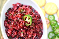 a white bowl filled with pomegranate on top of a table next to crackers