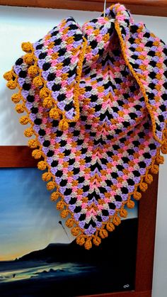 a crocheted blanket hanging from a hook on a wooden shelf next to a painting