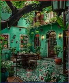 an outdoor dining area with green walls and potted plants on the floor, in front of a large tree