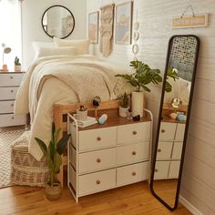 a bedroom with a bed, dresser and mirror in the corner next to a potted plant