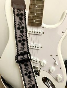 an electric guitar strap with black flowers on it, sitting in front of a white guitar