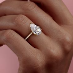 a woman's hand holding an engagement ring with a pear shaped diamond