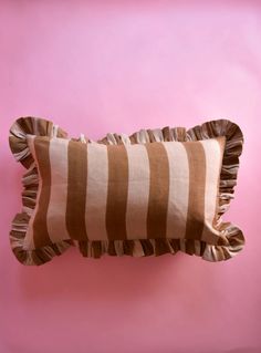 a brown and white striped pillow sitting on top of a pink wall with ruffled edges