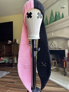 a pink and black knitted hat on top of a wooden stand in front of a fireplace