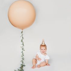 a baby sitting on the ground with a balloon