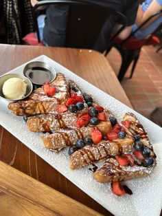 french toast with berries, blueberries and powdered sugar on a white platter