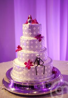 a three tiered wedding cake decorated with red flowers and skeleton figurines on top