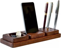 a cell phone, pen and watch on a wooden stand with two pens in it