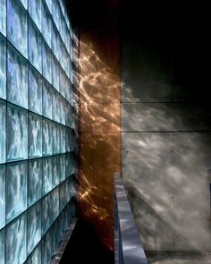 the reflection of clouds in glass blocks is seen on the wall next to a bench