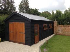 a black shed with wooden doors and windows on the side of a brick fenced in area