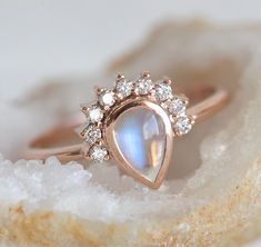 a rose gold ring with a rainbow colored stone in the center and small white diamonds around it